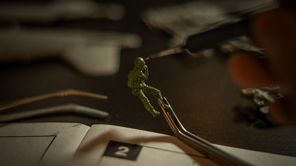 a small plastic soldier being held by tweezers and painted using a small and detailed paint brush