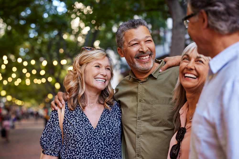 Group of happy senior friends sharing a moment outdoor while embrace. Older men and laughing women chatting together during a walk. Close up face of cheerful retirees enjoying time in a lively city street