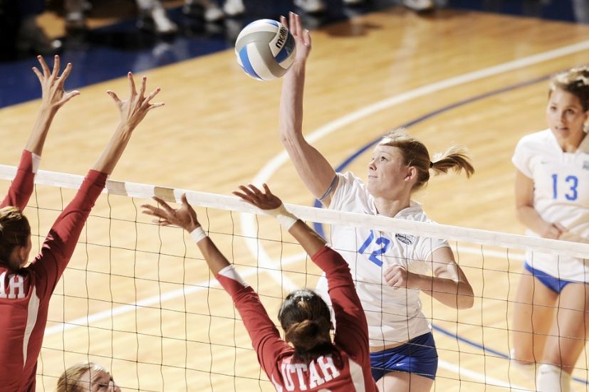 women playing volleyball, a woman in white shirt striking a volleyball to the opponents in red