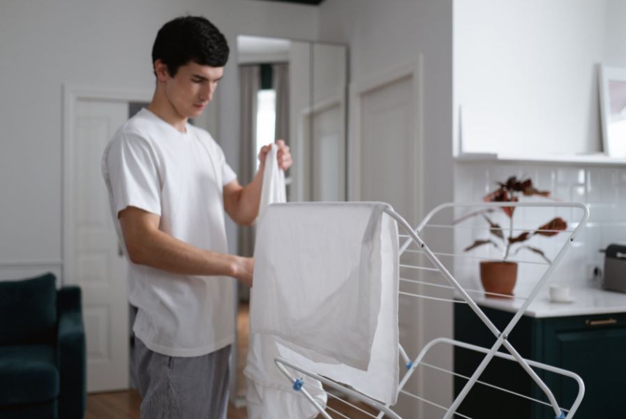 a man in a white shirt folding a white cloth inside the laundry room, white cloth drape on a hanging rack