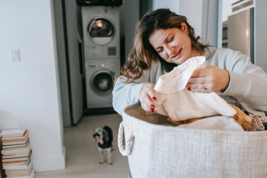a woman folding her laundry, a dog, stacked washing machine and dryer, laundry room
