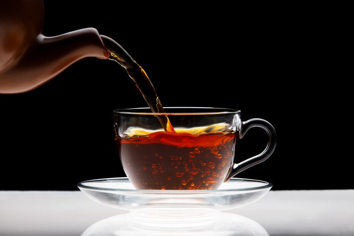 Pouring black tea into transparent cup isolated