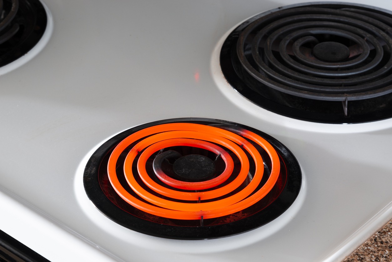 Horizontal shot of a white stove top with one hot burner and two off